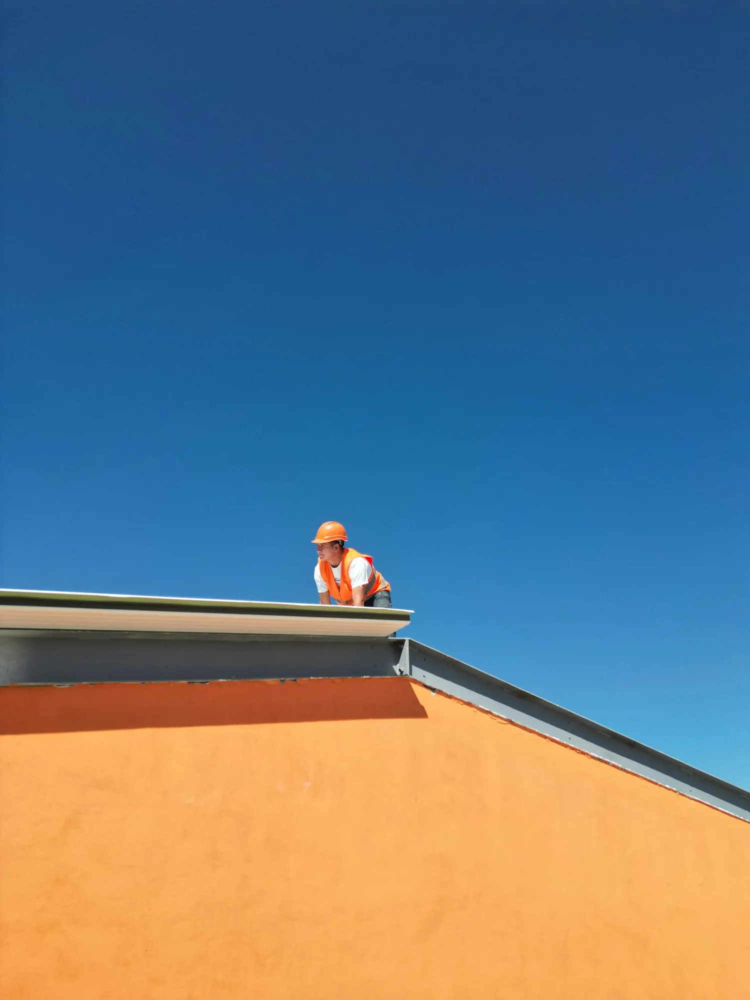 Roofer working on a roof edge against a clear sky